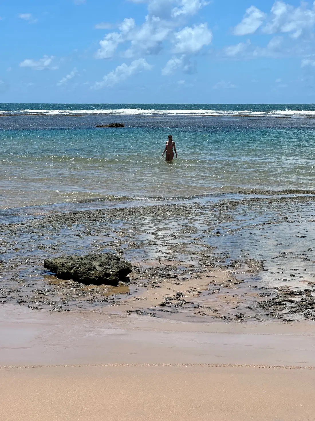 Piscinas naturais na maré baixa em Barra Grande, com uma pessoa na água e pedras na areia