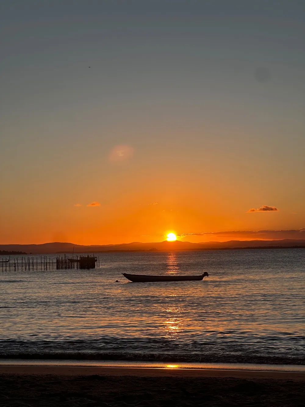Pôr do sol laranja sobre o mar de Barra Grande, com um barco na água